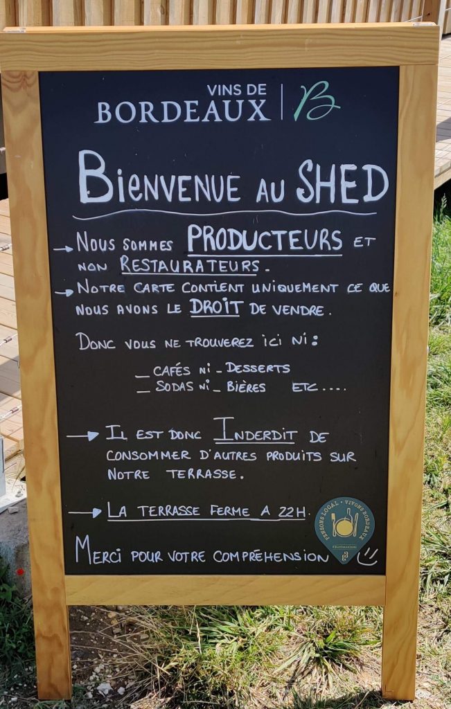 Panneau noir affichant les règles du Shed, précisant que c'est un producteur de Vins de Bordeaux et non un restaurateur, interdisant la consommation de produits extérieurs