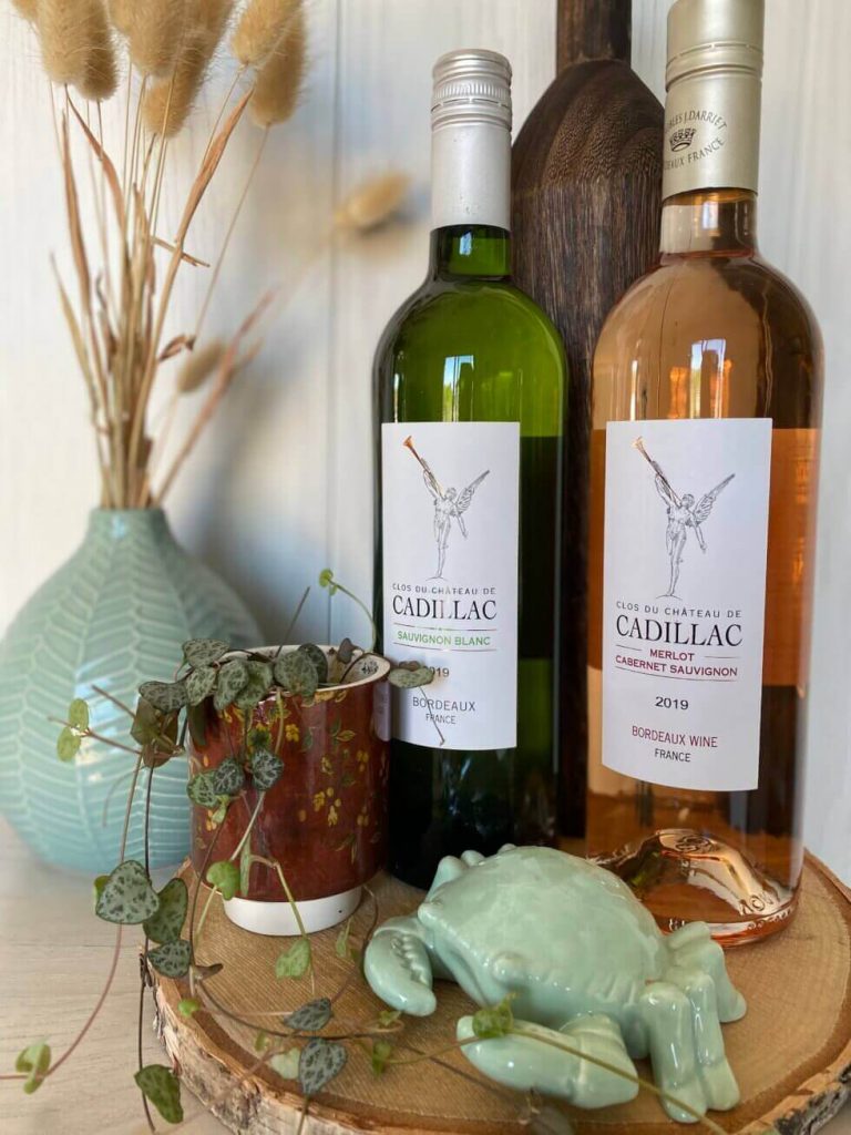 Deux bouteilles de vin Clos du Château de Cadillac, Sauvignon Blanc et Merlot Cabernet Sauvignon rosé, posées sur une souche de bois avec décoration marine et végétale